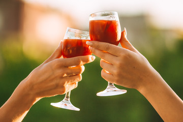 Cheers. Female hands cheering on sunset with red wine fresh sangria glasses with green sunny garden...