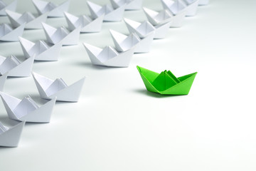 Leadership concept with Green paper ship standing out from the group of white ships on white...
