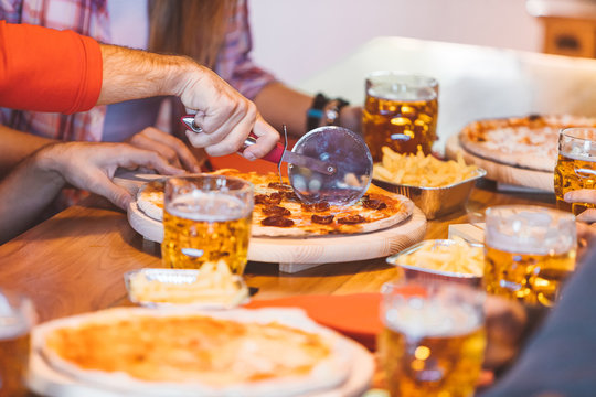 Group of college students cutting home made or take away pizza. Best friends dinning with pizza and beer. Close-up image with focus on cutter.
