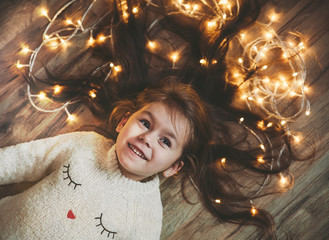 Cute little girl laying on flor with bright christmas garland in her hair.