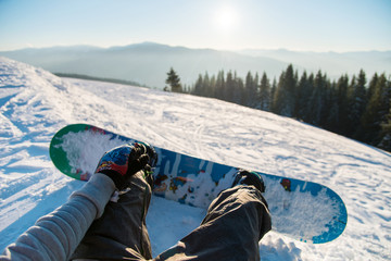 Point of view shot of a female snowboarder lying on the snow on the slope relaxing after riding, enjoying stunning view of winter mountains and sunset POV concept - obrazy, fototapety, plakaty