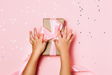 Child hands holding beautiful gift box on pink background
