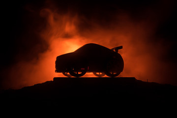 The car in the shadows with glowing lights in low light, or silhouette of sport car dark background.