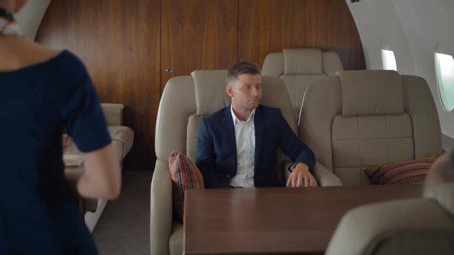 Businesspeople inside of private jet relaxing while flying and speaking with stewardess. She asked passengers about drinks and meal. Luxury service.