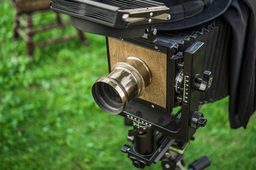 An old camera with legs stands on the street on the green grass. City event