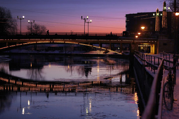 sunset scene in winter town with a bridge over a river and a parked bicycle