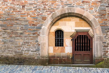 Old wall and the side door in the medieval castle in Bouzov. Stone fortress castle wall of a medieval castle, an old wooden closed arcade door with iron rivets. Place for text, copuspace.