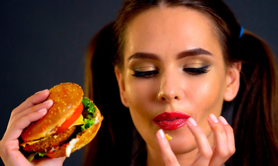 Woman bite big hamburger. Girl eat fast food and lick your fingers after eating.