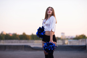 cheerleader with pompoms dancing outdoors on the roof at sunset