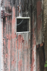 Close up of an old wooden shack door with a square window and peeling red paint.