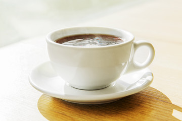 White cup of black tea on wooden table in a restaurant