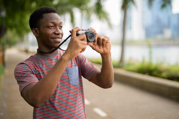 Young handsome African man taking pictures with camera in park