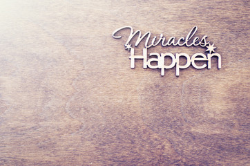 Inscription miracles happen on a wooden background. Concept of inspiration and hope.