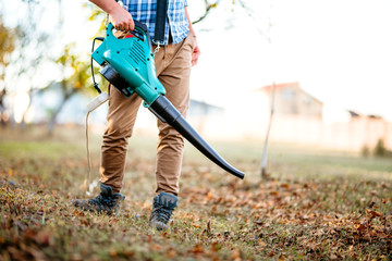 Gardener clearing up leaves using an electric leaf blower tool. Gardening details