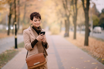 stylish young woman uses smartphone against background of autumn street
