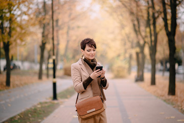 stylish young woman uses smartphone against background of autumn street