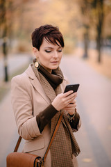 stylish young woman uses smartphone against background of autumn street