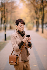 stylish young woman uses smartphone against background of autumn street