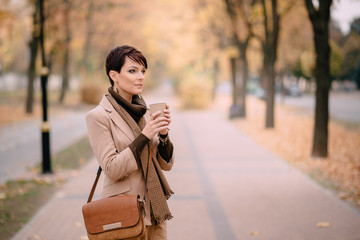 woman stands on background of autumn city and holds cup of coffee
