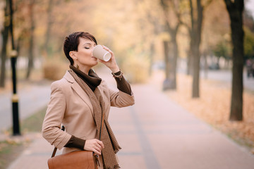 young stylish woman drinking coffee on background of autumn city