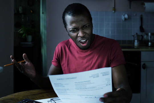 High Taxes Concept. Young Frustrated African American Man Looking At Utility Bill, Worried About Troubles With Mortgage Payment To Bank, Having Serious Problems With Debt