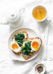 Fried spinach, labne, boiled eggs sandwiches and green tea - delicious healthy breakfast or snack on a light background, top view
