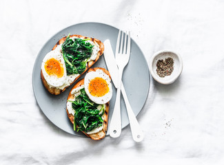Fried spinach, labne and boiled eggs sandwiches - delicious healthy breakfast or snack on a light background, top view