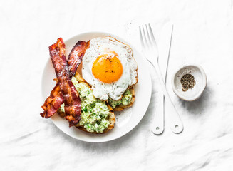 Healthy nutritious breakfast or snack - avocado toast, bacon and fried egg on light background, top view