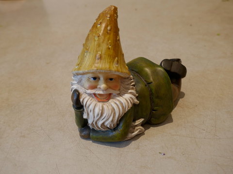 Garden Gnome lies on his stornach and laughs. Close-up.Isolated against neutral background