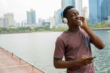 Happy African man in park using mobile phone and listening music with headphones