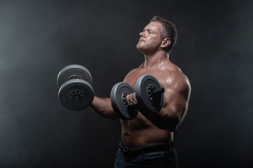 Naklejka na ściany i meble muscular man trains with dumbbells on black background in smoke