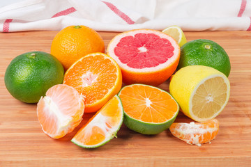 Whole, halves and slices of various citrus on wooden surface