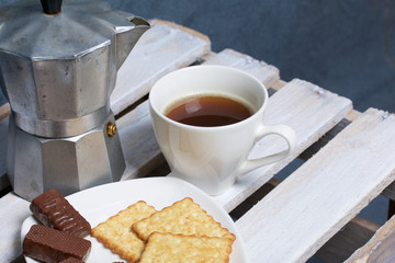 Coffee in a geyser coffee maker cookie and candy on a saucer stand on a wooden box.