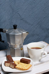 Coffee in a geyser coffee maker cookie and candy on a saucer stand on a wooden box.