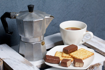 Coffee in a geyser coffee maker cookie and candy on a saucer stand on a wooden box.
