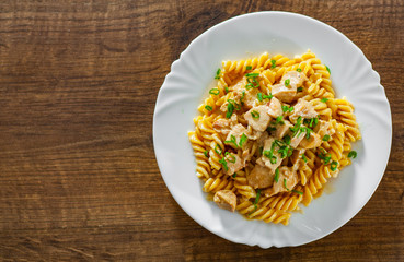 Sliced fried chicken fillet in a creamy sauce with fusilli pasta in white plate on wooden table