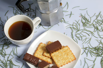 Coffee, cookie and candy on a saucer stand on a wooden box. On a white background sprinkled with fir needles.