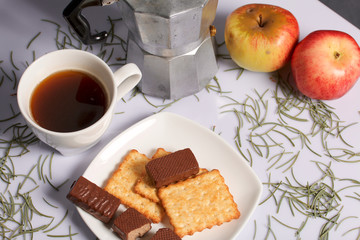 Coffee, cookie, apples and candy on a saucer stand on a wooden box. On a white background sprinkled with fir needles.