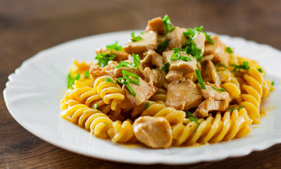 Sliced fried chicken fillet in a creamy sauce with fusilli pasta in white plate on wooden table