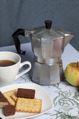 Coffee, cookie, apples and candy on a saucer stand on a wooden box. On a white background sprinkled with fir needles.