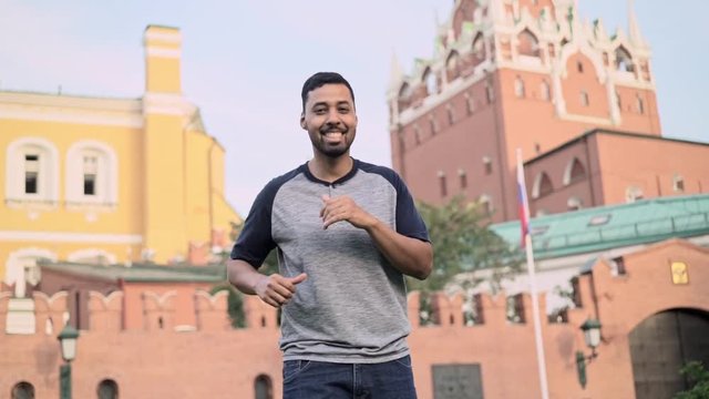 Cheerful hispanic guy wearing gray t shirt dancing in the Red Square in Russia on summer day. Handheld slow motion medium shot