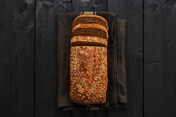 Loaf of sliced whole wheat bread on dark dishtowel over black wooden table. Top view with copy...