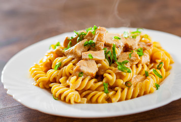 Sliced fried chicken fillet in a creamy sauce with fusilli pasta in white plate on wooden table