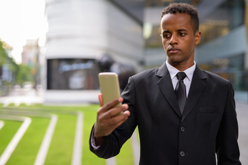 Successful young African businessman using mobile phone outdoors