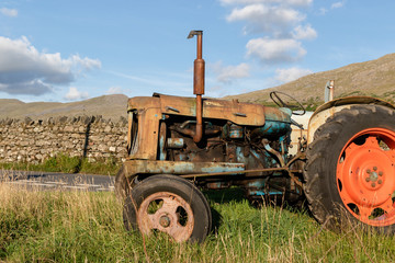Old abandoned rusty agricultural tractor in a grass field