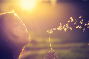 Junges Mädchen bläst Samen einer Pusteblume, Sonnenuntergang im Herbst mit Textfreiraum