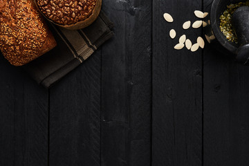 Various crusty whole wheat bread with pumpkin seeds, mortar and pestel on black wooden table. Top view with copy space for text, menu or recipes.