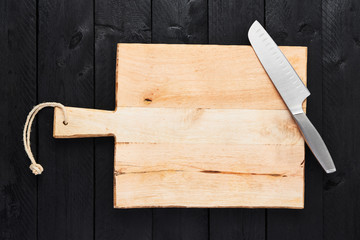 Top view of chopping board with stainless steel vegetable knife on black wooden table with copy space.