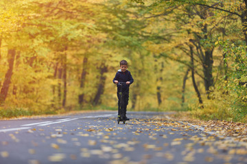 Cute boy riding scooter, outdoor in autumn environment on sunset warm light