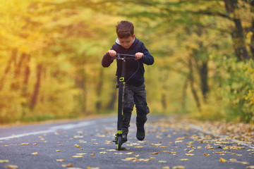 Cute boy riding scooter, outdoor in autumn environment on sunset warm light